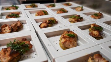 A variety of small dishes on white plates. Each dish contains grilled meat and is garnished with fresh herbs.
