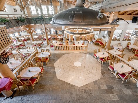 A cozy restaurant with stylish wooden paneling and adjoining dining areas. The tables are lovingly set, and the lighting concept creates an inviting atmosphere.