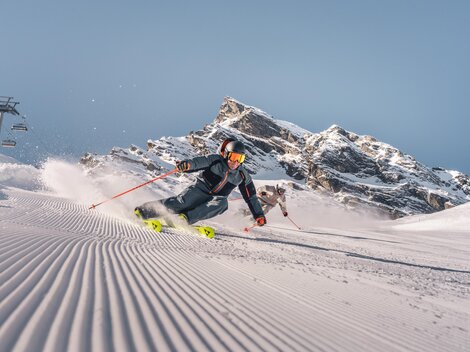 A skier glides through fresh snow in the mountains. In the background, impressive rocks and a blue sky can be seen.