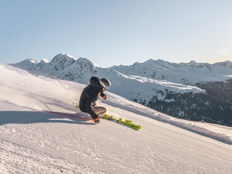A skier glides over a snow-covered slope in the mountains. In the background, majestic mountains and a clear sky can be seen.
