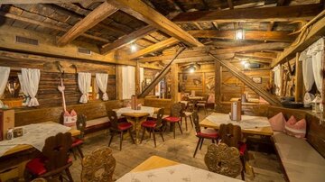 A cozy restaurant with wooden walls and rustic tables. Red chairs and decorative curtains create an inviting atmosphere.