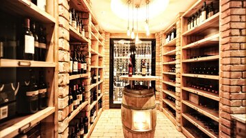 An elegant wine cellar with shelves full of wine bottles. In the center stands a barrel-shaped piece of furniture.