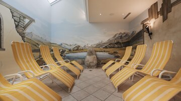 Ein moderner Wellnessraum mit gelb gestreiften Liegen. Die Wände sind mit einer malerischen Berglandschaft dekoriert.