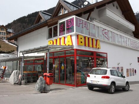 A Billa supermarket with a modern facade and large windows. In front of the store, there is a white car in a parking lot.