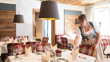 A cozy restaurant with an inviting atmosphere. A waitress sets the table with elegant glasses and napkins.