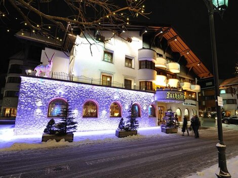 A charming hotel in a snowy town at night. The facade is illuminated with colorful lights, creating a festive atmosphere.