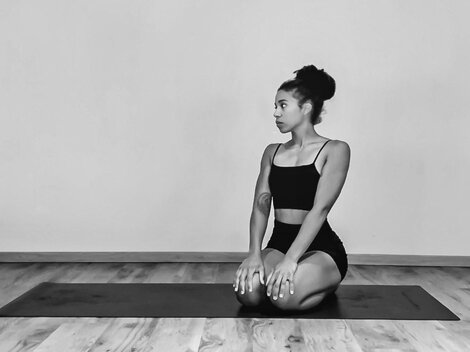 Eine Person sitzt in einer Yogaposition auf einer Matte. Der Raum ist schlicht und minimalistisch.