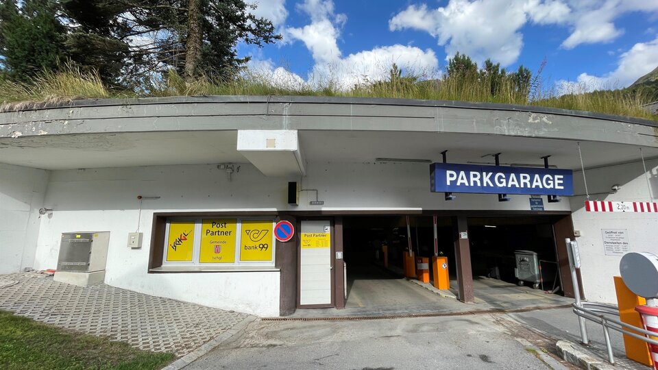 Eine Parkgarage mit einem Eingang und einem Schild, das "PARKGARAGE" anzeigt. Der Himmel ist blau mit einigen Wolken.