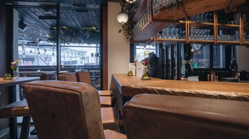 Eine stilvolle Bar mit Holzinterieur und modernen Sitzmöbeln. Große Fenster sorgen für viel Tageslicht und eine einladende Atmosphäre.