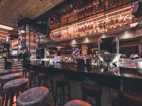 A modern bar with an elegant counter and stylish bar stools. The lighting and decoration create an inviting atmosphere.