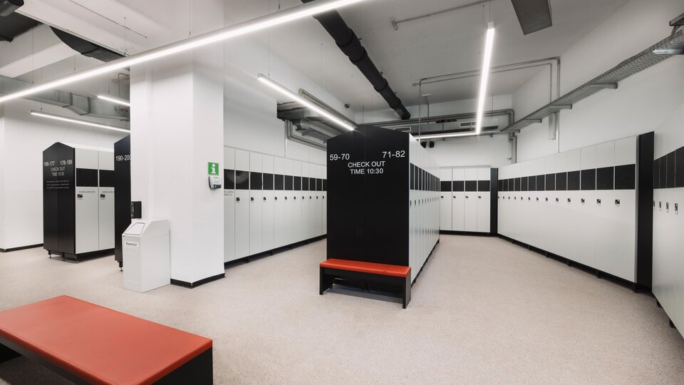 A modern changing room with several lockers in black and white. In the middle is a bench in orange.