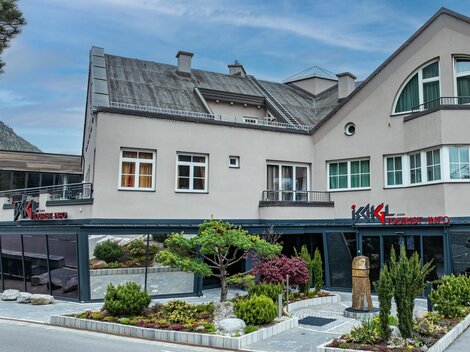 Ein modernes Gebäude mit einem Restaurantbereich und gepflegten Gartenanlagen. Die Architektur ist ansprechend und die Umgebung lädt zum Verweilen ein.