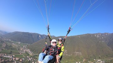 Ein Paragliding-Erlebnis über einer malerischen Landschaft. Die Aussicht umfasst grüne Täler und Berge unter einem klaren blauen Himmel.
