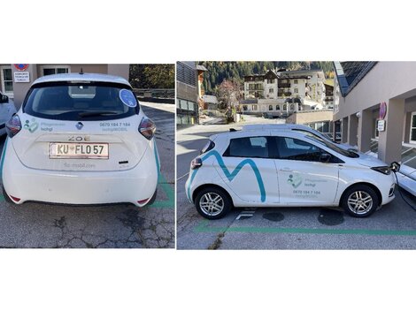 Ein weißes Auto mit Werbung auf der Seite parkt in einer Stadt. Die Umgebung zeigt Wohngebäude und eine saubere Straße.